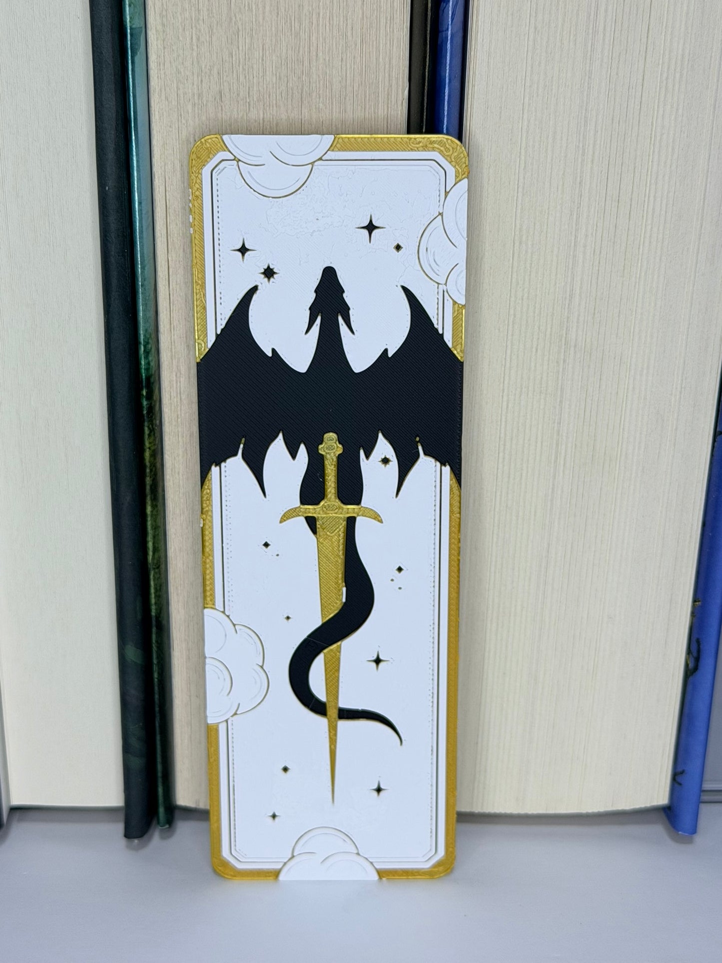 Bookmark with a black dragon and gold sword design on a white background