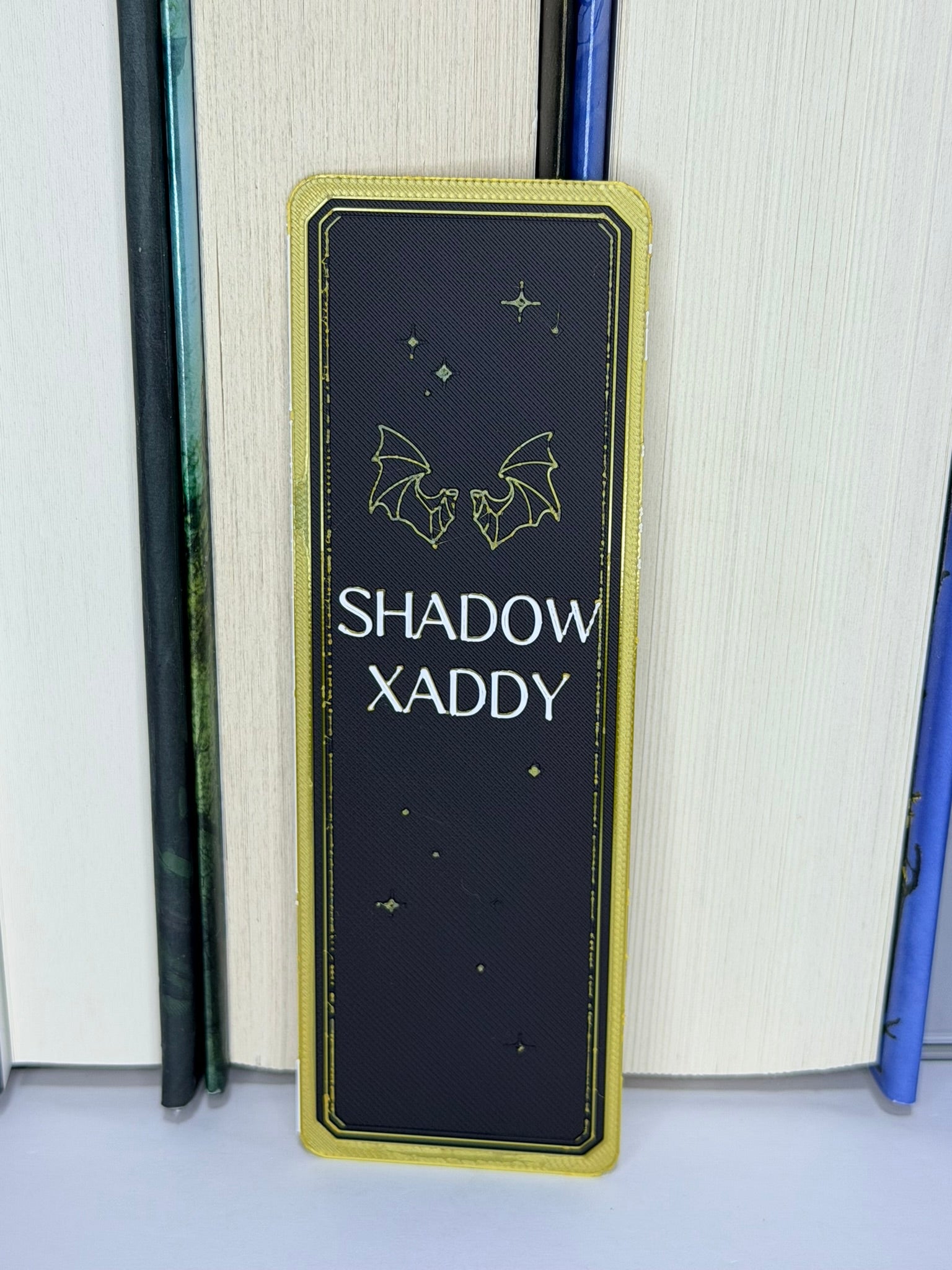 Book with a 'Shadow Xaddy' bookmark featuring bat illustrations on a white surface.